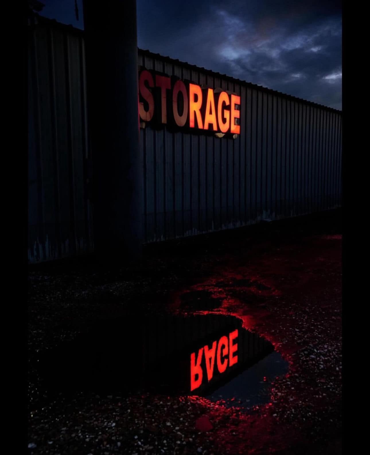 This meme is a humorous image of a storage facility at night, with a sign reading "Storage" and a puddle of water reflecting the sign. The sign is reflected in the puddle, but it's distorted and reads "Storace" instead of "Storage". The meme is likely poking fun at the idea of a storage facility being a place where things are stored, but the word "Storace" sounds like "store" and "ace", implying that the storage facility is actually a place where people can store their "aces" (a clever play on words).